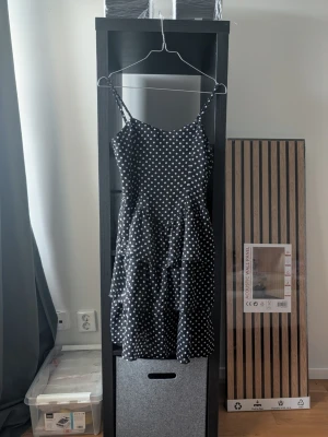 Svart prickig klänning SisterSpoint - Svart kortklänning från SisterSpoint med vita prickar och tunna axelband. Klänningen har en figurnära passform och vol sopartade detaljer i kjolen. Perfekt för dig som gillar en lekfull och trendig stil.