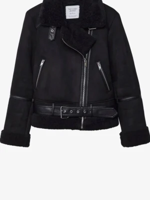 Svart teddy/mocka jacka med bälte och dragkedja - Svart teddyjacka med stora slag, mysig fuskpäls på insidan och detaljer i skinnimitation. Jackan har sned dragkedja, två fickor med dragkedja och ett brett bälte i midjan. Perfekt för kalla dagar och ger en cool look. 