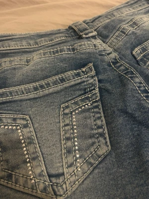 Blå bootcut jeans med nitar - Snygga ljusblå bootcut jeans med dekorativa nitar på bakfickorna från gina young u storlek 152. Jeansen har klassisk femficksmodell, normal midja och är tillverkade i mjukt denimtyg. Perfekta för dig som gillar en retroinspirerad look med extra detaljer. Aldrig använt 🥰