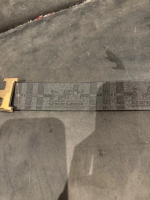  svart läderbälte - Snyggt svart bälte  läder med klassiskt guldigt spänne. Bältet har diskret logga och mönster längs remmen. Perfekt accessoar för att lyfta din outfit med en lyxig touch. PRIS KAN DISKUTERAS 