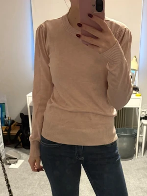 Ljusbeige stickad tröja med puffärm - Säljer en ljusbeige stickad tröja med puffärm och rund halsringning. Tröjan har långa ärmar och ribbade muddar vid ärmslut och nederkant. Perfekt att matcha med jeans för en clean och enkel look.
