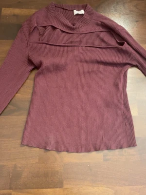 Vinröd stickad tröja från LeGer - Trendig vinröd stickad tröja från LeGer med ribbad struktur och unik cut-out detalj vid nyckelbenen. Tröjan har lång ärm och en mjuk, följsam passform som passar perfekt till jeans eller kjol. Materialet känns skönt mot huden och ger en modern look.