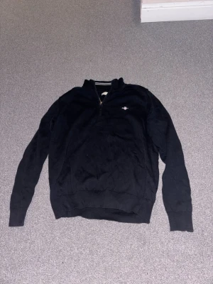 Gant halvzip tröja svart - Svart långärmad tröja med halv dragkedja och liten broderad logga på bröstet. Tröjan har ribbade muddar vid ärmslut och nederkant samt en klassisk ståkrage. Perfekt för en avslappnad men stilren look. Är i storlek 164 men passar också XS, pris kan diskuteras!
