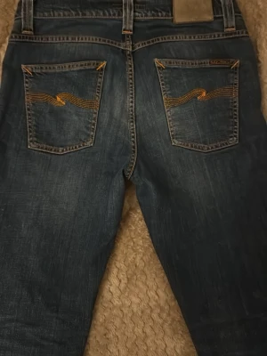 Nudie jeans lean dean  - Snygga blå jeans med klassisk femficksdesign och kontrastsömmar på bakfickorna. Jeansen har en rak passform och subtila slitningar framtill. Perfekta för en avslappnad och trendig look.