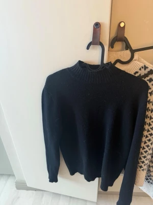 Svart stickad tröja från Vila - Snygg svart stickad tröja från Vila med hög ribbad krage och långa ärmar. Tröjan har en enkel och stilren design som passar perfekt till jeans eller kjol. Materialet känns mjukt och bekvämt mot huden.