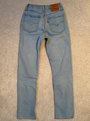 Levi's 501 ljusblå jeans straight fit. - Säljer ett par klassiska ljusblå Levi's 501 jeans med raka ben och femficksmodell. Storlek 16 år=164/170cl. Jeansen har normal passform och är tillverkade i mjuk bomullsdenim. Justerbar midja med resår och knapp.Något sliten tagg på baksidan(se bild). Annars i fint använt skick.