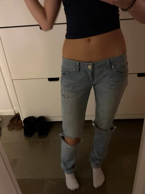 Ljusblå ripped jeans från My God - Säljer ett par ljusblå jeans från My God med slitningar och hål på knäna. Modellen har låg midja och klassisk femficksdesign. Jeansen är i mjuk bomull och har en avslappnad passform som ger en cool och trendig look.