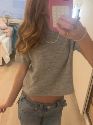 Grå kortärmad stickad tröja - Superfin grå croppad stickad topp med korta ärmar. Enkel och stilren design som passar perfekt till jeans eller kjol. Mjuk och skön att ha på sig, perfekt för dig som gillar en avslappnad men trendig look.