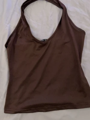 Brun halterneck topp från SHEIN - Snygg brun halterneck topp från SHEIN. Toppen är ärmlös och har en tight passform med enkel design, perfekt att styla till olika outfits. Tillverkad i mjukt och stretchigt syntetmaterial.