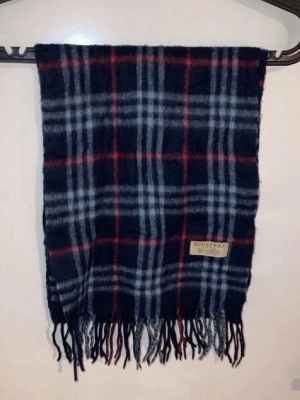 Rutig halsduk från Burberry i ull - Mörkblå halsduk från Burberry med klassiskt rutmönster i vitt och rött. Halsduken har fransar i ändarna och en tygpatch med Burberry-logga. Tillverkad i mjuk ull som håller dig varm och snygg under kalla dagar.