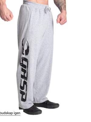 Grå mjukisbyxor från GASP, DM för bilder - Säljer ett par grå mjukisbyxor från GASP med bred passform och snörning i midjan. Byxorna har stort svart tryck längs ena benet och fickor på sidorna. Tillverkade i mjukt bomullsmaterial, perfekta för chill eller gymmet.