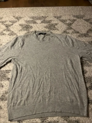 Ljusgrå rundhalsad tröja från H&M - En stilren ljusgrå tröja från lager157 med rund halsringning och korta armar .Tröjan är tunnstickad och har ribbade muddar vid ärmslut och nederkant. Perfekt för lager-på-lager och enkel att matcha med olika outfits.