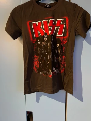 KISS t-shirt från H&M Young - Svart t-shirt från H&M Young med stort KISS-tryck och bandmedlemmarna på framsidan. T-shirten har korta ärmar och rund hals. Perfekt för dig som gillar rock och vill sticka ut med en cool bandtröja.