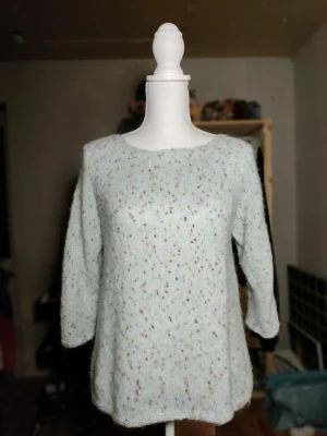 Ljusblå/turkos handstickad tröja - Handstickad ljusblå stickad tröja med rund hals och trekvartsärmar. Tröjan har en popcorn effekt i flera färger. Tillverkad i ett fluffigt garn (polyester, ull, akryl). Bredd 41, Längd 62 (cm)