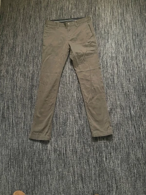 Beiga chinos med rak passform - Snygga beiga chinos med rak passform och klassisk design. Byxorna har framfickor, bälteshällor och två bakfickor med knapp. Perfekta för en clean och stilren look. Materialet känns mjukt och är troligtvis bomull eller en bomullsblandning.Var inte rädd för att skicka om du har någon fråga eller vill ha fler bilder!