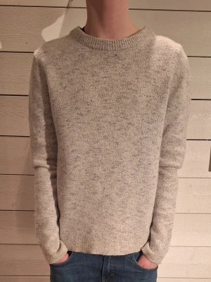 Ljusgrå melerad stickad tröja - En stilren ljusgrå melerad stickad tröja med rund halsringning och ribbade muddar vid ärmslut och nederkant. Tröjan har en rak passform och är perfekt för lager på lager. Materialet känns mjukt och bekvämt mot huden. Modelen är 172 cm!