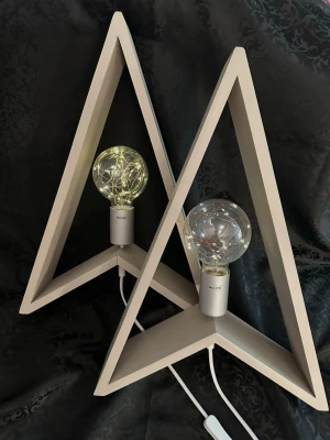 Beige trekantiga lampor från Star Trading - Två stilrena lampor från Star Trading i form av trekantiga ramar i beige trä. Lamporna har stora glödlampor med dekorativa LED-slingor inuti och vit sladd med strömbrytare. Perfekt som mysig belysning i fönster eller på hylla. Lampor i bra skick. 51 cm längd 