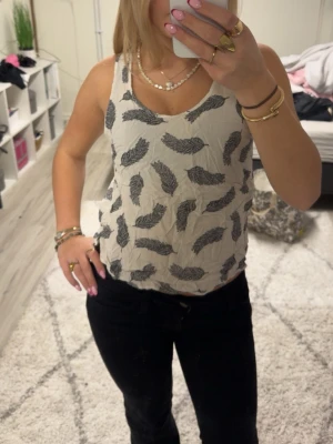 Vit linnetopp med svart fjädermönster H&M - Säljer en vit linnetopp från H&M i storlek 38. Toppen har ett svart fjädermönster över hela och är ärmlös med rundad halsringning. Materialet är lätt och luftigt, perfekt för varma dagar. Passformen är normal och toppen är något croppad i modellen.