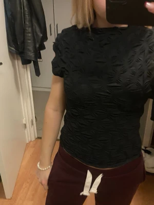 ZARA - Säljer en svart topp med korta ärmar och coolt strukturerat mönster som ger en unik look. Toppen är figurnära och har en lätt croppad passform. Materialet känns mjukt och stretchigt, perfekt för att lyfta din outfit med lite extra edge.