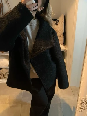 Svart teddyjacka med oversized krage - Säljer en svart teddyjacka med stor, bred krage och avslappnad passform. Jackan är gjord i ett mjukt och fluffigt material som ger en cool och trendig look. Perfekt för dig som gillar oversized stil och vill ha något som sticker ut.