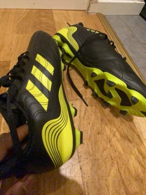 Adidas Copa fotbollsskor svart/gul - Säljer ett par Adidas Copa fotbollsskor i svart och neon-gult. Skorna har klassiska tre ränder på sidan, snörning och mönstrad sula för bra grepp på planen. Tillverkade i skinn med coola grafiska detaljer och rund tå. Perfekta för dig som vill sticka ut på fotbollsplanen.