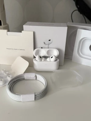 AirPods Pro - Säljer ett par Apple AirPods Pro 2 i mycket fint skick, komplett med originalkartong, laddningskabel, extra öronproppar. Hörlurarna är rena och utan repor eller skador. Perfekt för dig som vill ha trådlösa hörlurar med aktiv brusreducering. Används till allt dom träning, samtal och musik