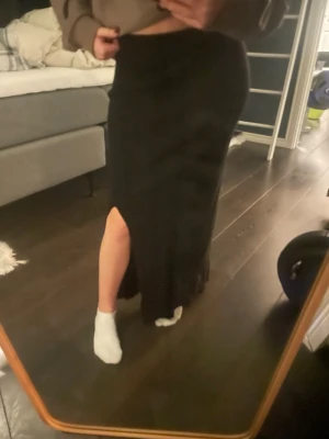 Svart långkjol med slits - Säljer en svart långkjol med snygg slits på sidan. Kjolen har en rak och enkel design som sitter bekvämt i midjan. Materialet känns mjukt och följsamt, perfekt för dig som gillar stilrena plagg med lite edge.