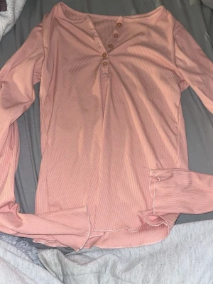 Rosa ribbad långärmad topp med knappar -  ljusrosa långärmad topp med ribbad struktur och  knappar framtill. Toppen har en mjuk och stretchig känsla. 
