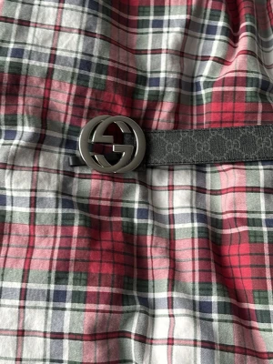 Svart Gucci skinnväst med bälte - Säljer en svart väst från Gucci med ett snyggt bälte i skinn och ikoniskt GG-spänne i silver. Västen har en klassisk och stilren look som passar perfekt till streetwear. Bältet är dekorerat med diskret GG-mönster och ger en lyxig touch. Helt äkta är den köpt från Gucci 
