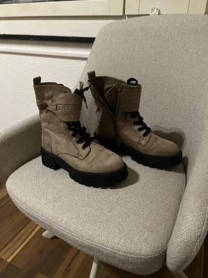 Beige boots från Esprit med snörning - Säljer ett par beige boots från Esprit i mocka med grov svart sula och snörning. Skorna har rund tå, dragkedja på sidan och ett brett spänne med logga upptill. Perfekta för dig som gillar chunky stil och vill ha något som sticker ut.