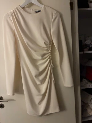 Vit klänning från Zara - Snygg vit kortklänning från Zara med lång ärm. Dragkedja bak. Figurnära. Aldrig använt. Ca 90 cm lång. 