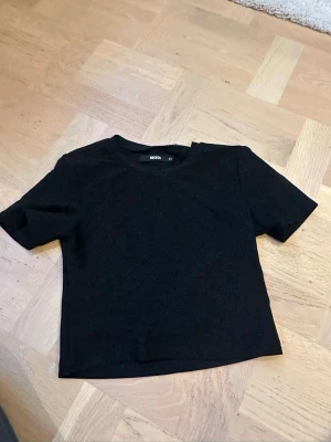 Svart glittrig T-shirt från BikBok  - Säljer en svart glittrig T-shirt från BikBok i storlek XS. Toppen har korta ärmar och en rak, croppad passform. Prefekt till byrå. Pris kan diskuteras.