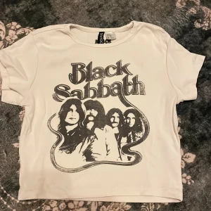 Vit Black Sabbath t-shirt H&M Divided - Vit t-shirt från H&M Divided med Black Sabbath-tryck. Perfekt för dig som gillar bandtröjor och vill ha en cool och avslappnad stil.