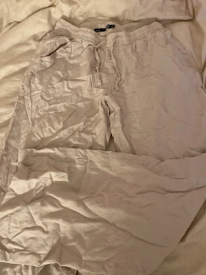 Beige mjukisbyxor från 157, XS - Säljer ett par beige linnebyxor från Lager 157 i storlek XS. Byxorna har elastisk midja med snörning och praktiska sidofickor. Sköna och avslappnade, perfekta för chill dagar. Materialet känns mjukt och lätt mot huden.