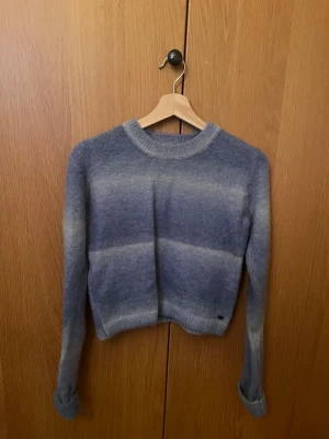 Blå stickad tröja från Pull&Bear - Mysig blå stickad tröja från Pull&Bear, Pacific Republic Teen Department. Tröjan har ett randigt mönster i olika blå nyanser och är långärmad med rund hals. Perfekt för kyliga dagar och enkel att matcha med jeans eller kjol. Endast använd en gång.