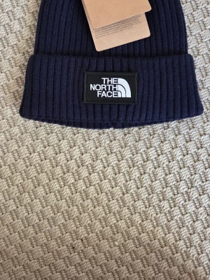 Mörkblå ribbad väst från The North Face - Snygg mörkblå väst från The North Face med ribbad struktur och tydlig logotyp framtill. Västen har en klassisk, enkel design som gör den lätt att matcha med olika outfits. Perfekt för dig som gillar stilrena och funktionella plagg.