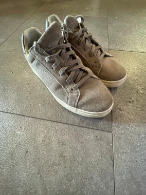 Unified mockaskor - Säljer ett par grå sneakers från Unified med snörning och rund tå. Skorna har ovandel i mocka och detaljer i skinn på hälen med tryckt UNFD. på baksidan. Snygg och stilren design med platt sula, perfekt för dig som gillar enkel streetstil.