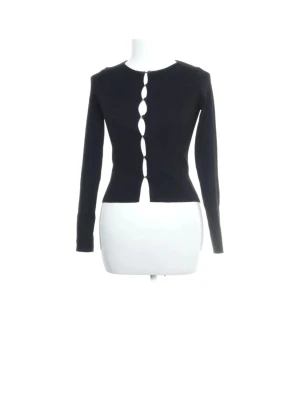 Svart ribbad kofta med cut-out detaljer - Säljer en svart ribbad kofta med lång ärm och unika cut-out detaljer längs knäppningen framtill. Figurnära passform och rund halsringning. Perfekt för dig som vill ha något stilrent men ändå edgy.