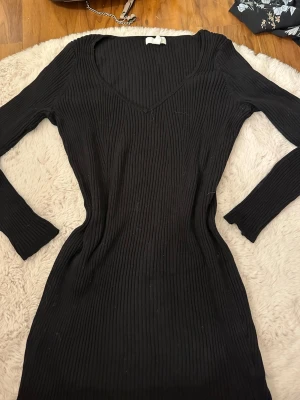 Svart ribbad långärmad klänning - Säljer en svart, ribbad klänning med lång ärm och v-ringad hals. Klänningen är figurnära och har en snygg, enkel design som passar perfekt för dig som gillar stilrena plagg. Materialet känns mjukt och stretchigt, vilket gör den bekväm att bära hela dagen.