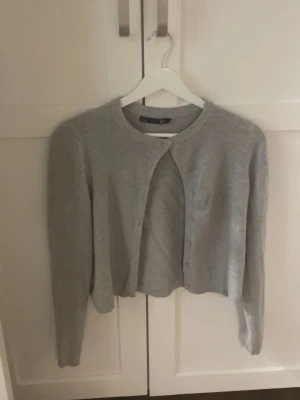 Grå kofta från lager157 med knappar - Säljer en ljusgrå, croppad kofta från lager157 i storlek S. säljer eftersom den ej passar. Storleken är S men passar bra som XS till och med XXS
