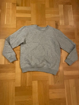 Grå sweatshirt från Kappahl - En basic grå sweatshirt från Kappahl i storlek 158/164. Tröjan har rund hals, ribbade muddar vid ärmslut och nederkant samt är långärmad. Perfekt för chill dagar eller när du vill ha en enkel och clean look.