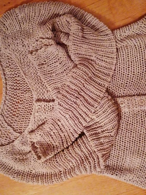 Beige stickad kofta med knappar - Säljer en beige stickad kofta med lång ärm och rund hals. Koftan har en rad med knappar framtill och är gjord i ett grovt stickat material som ger en chill och avslappnad vibe. Perfekt att slänga över en t-shirt eller linne när det blir lite kyligt.