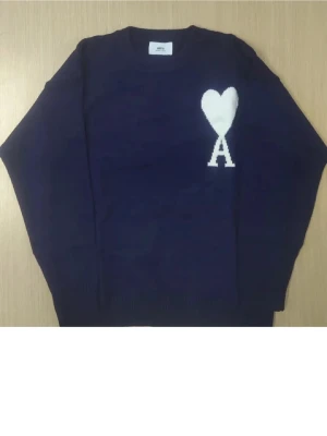 Mörkblå stickad tröja från Ami - Snygg mörkblå stickad tröja från Ami med vit hjärtapplikation och bokstaven A på bröstet. Rund hals och långa ärmar, perfekt för dig som gillar stilrena detaljer och vill ha något som sticker ut lite extra.