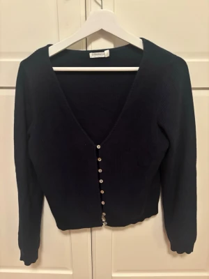 Mörkblå kofta från Stradivarius - Snygg mörkblå kofta från Stradivarius med v-ringad hals och långa ärmar. Koftan är stickad och har en rad små knappar framtill. Perfekt att slänga över en topp för en chill look. Storleken är L men skulle säga xs-s 