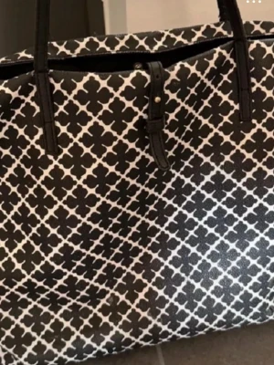 Svartvit shoppingväska By Malene Birger - Stor och rymlig shoppingväska från By Malene Birger med svart och vitt grafiskt mönster. Väskan har svarta handtag och detaljer, samt ljus insida med logotyp. Perfekt för dig som gillar stilrena och trendiga accessoarer.