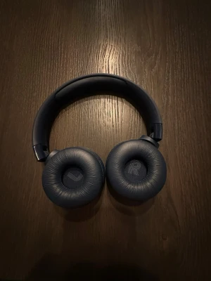 JBL trådlösa over-ear hörlurar - Snygga blå JBL over-ear hörlurar med trådlös anslutning. Mjuka öronkuddar och tydliga knappar för enkel kontroll. Hörlurarna ser ut att vara i gott skick utan synligt slitage eller defekter. Perfekt för musik, samtal och långvarig användning.