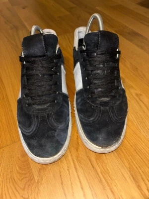 Valentino flycrew  - Säljer ett par stilrena sneakers i svart och vitt med ovandel i mocka och detaljer i skinn. Skorna har svarta snören, vit sula och klassisk låg profil. Perfekta för dig som gillar en enkel men snygg look till vardags.