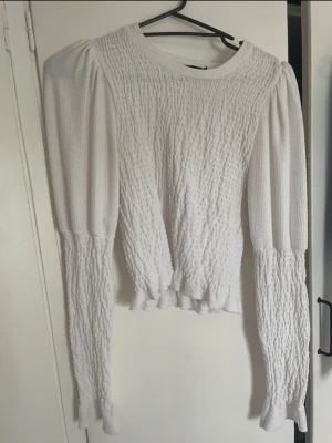 Vit blus med puffärm och struktur - Säljer en vit blus med puffiga långärmar och snyggt strukturerat tyg. Blusen har rund halsringning och volangdetaljer vid ärmslut och nederkant. Perfekt för dig som gillar en trendig och feminin stil.