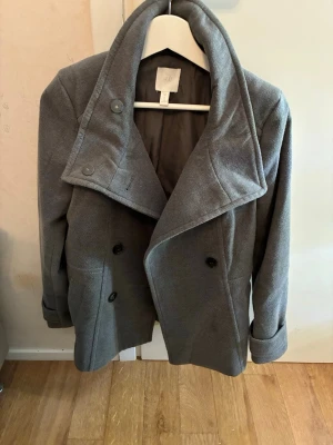 Grå skepparkavaj från H&M - Snygg grå skepparkavaj från H&M med bred krage och dubbelknäppning framtill och två sidofickor OBS En knapp  saknas!
