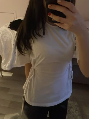 Vit topp med knyt i midjan - Säljer en vit T-shirt från Nelly . Toppen har snygg knytning i midjan som ger en cool och feminin siluett. den går att ha på två olika sätt, genom att knyta i sidorna eller i fram och bak. Pris kan diskuteras💕